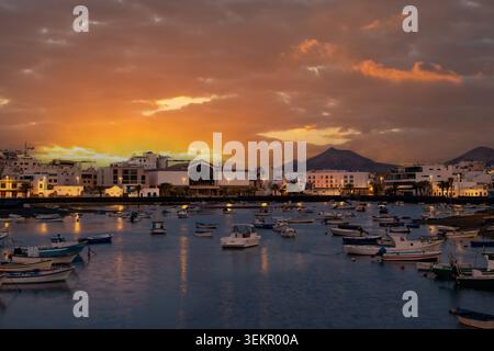 Boote schweben in der Lagune von Arrecife, Lanzarote, während der Tag in die Nacht verwandelt wird. Gebäude säumen die Uferpromenade und reflektieren die Lichter der Stadt auf dem Wasser. Stockfoto