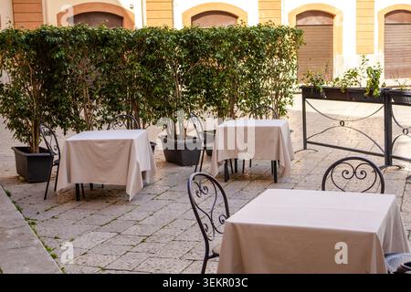 Cafétische im Freien in einer ruhigen Straße in Palermo, Sizilien. Gemütliche mediterrane Atmosphäre mit sanftem Licht und leerem Sitzbereich. Konzept des Fahrens, langsam Stockfoto