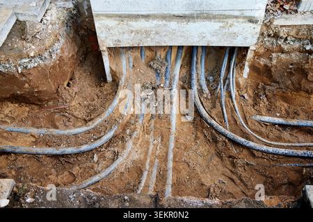 Unterirdische Stromkabel und Versorgungsleitungen, die während der Straßenbauarbeiten in der Stadt in einem Schottergraben ausgesetzt sind. Stockfoto