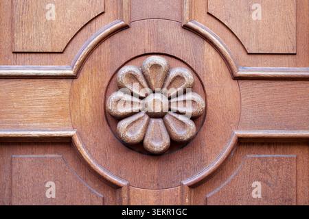 Eine Nahaufnahme einer geschnitzten Holzblume auf einer braunen Vintage-Tür oder Möbelplatte. Stockfoto