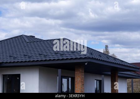 Ein neues Haus mit schwarzem Dach und großen Fenstern wird gebaut. Dunkle Wolken füllen den Himmel darüber. Diese Szene spielt in einem Wohngebiet während des Tageslichts Stockfoto