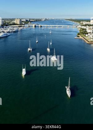 Blick aus der Vogelperspektive auf Segelboote und Luxusyachten, die auf dem ruhigen blauen Wasser des Intracoastal Waterway nahe einer Brücke unter klarem Himmel in Palm Beach ankern Stockfoto