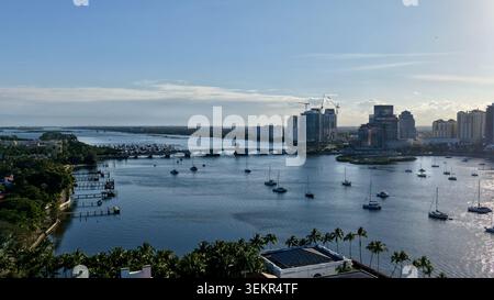 Aus der Vogelperspektive auf Segelboote, die im ruhigen Wasser nahe der Skyline der Stadt ankern, und eine Brücke unter einem klaren blauen Himmel in Palm Beach, Florida, USA. Stockfoto