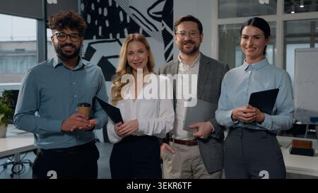 Multiethnisches Business-Team posiert im Büro vier multiethnische Geschäftsleute Diversity-Kollegen stehen in einer Agentur und lächeln zusammen Stockfoto