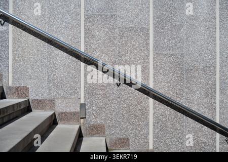 Minimalistische Stadtarchitektur mit Betontreppen, glänzendem Geländer und Marmorwand. Seitenansicht der Außentreppe mit Chrom-Handlauf an einem sonnigen Tag. Stockfoto