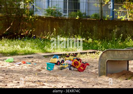 Bunte Plastikspielzeug-Trucks und Eimer liegen an einem sonnigen Tag in einem Sandkasten auf einem Kinderspielplatz im Freien. Stockfoto