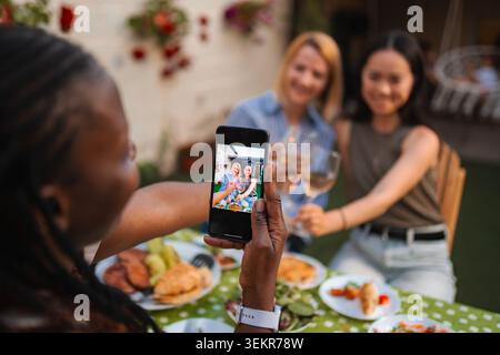 Frau, die ein Smartphone von glücklichen Freunden fotografiert, die jubeln Stockfoto
