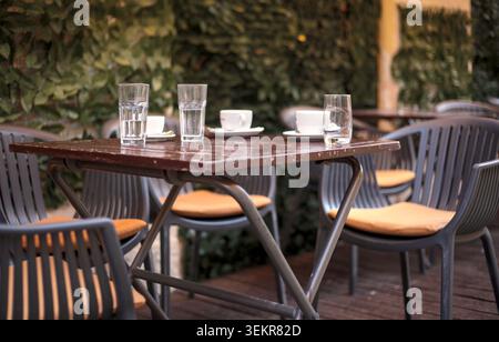 Eine gemütliche Terrasse im Freien mit dunklen Holztischen und grauen Plastikstühlen mit bequemen orangefarbenen Kissen. Stockfoto