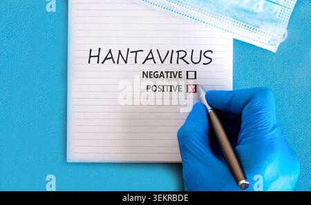 Hantavirus medizinisches Symbol. Konzeptworte Hantavirus positiv auf schöner weißer Note. Wunderschöner blauer Hintergrund. Arzthand in blauem Medizinhandschuh. Ich Stockfoto