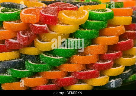 Nahaufnahme von gestapelten, farbenfrohen, mit Zucker überzogenen Fruchtgelees mit Zuckerkristallen und strukturierter Oberfläche – lebendiger Süßwarenhintergrund für Lebensmittel Stockfoto