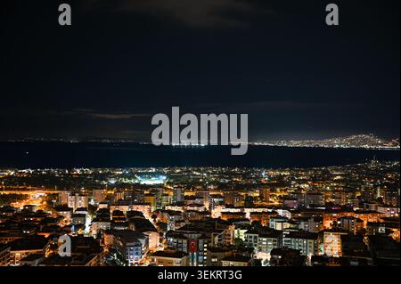 Nächtliche Panoramansicht der Küste von Izmir und der Stadtlichter entlang des Meeres, Langzeitbelichtetes urbanes Nachtbild in der Türkei. Stockfoto