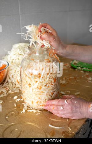 Hausgemachtes Sauerkraut in einem Glasgefäß von Hand in einer Küche, in der fermentierter Kohl zubereitet wird Stockfoto