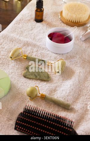 Grüne Steinrollen liegen auf einem beigefarbenen Handtuch über dem Holztisch, umgeben von Pinsel und Glas Stockfoto