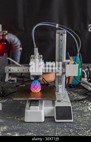 Desktop-3D-Drucker, der farbenfrohe geometrische Objekte mit leuchtendem Farbverlauf von violett zu gelb erstellt und die fortschrittliche Technologie für den mehrfarbigen Druck hervorhebt Stockfoto
