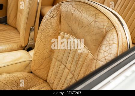 Die angewinkelte Nahaufnahme konzentriert sich auf das stark gefaltete, braune Ledermaterial eines Oldtimer-Eimersitzes, das eine satte Retro-Textur und eine satte Retro-Textur aufweist Stockfoto