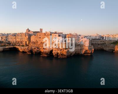 Blick aus der Vogelperspektive auf die historischen weißen Gebäude auf Kalksteinklippen mit Blick auf die Adria bei Sonnenuntergang Polignano a Mare, Apulien, Italien. Stockfoto