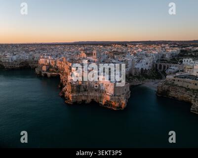 Aus der Vogelperspektive der historischen weißen Gebäude auf Kalksteinklippen mit Blick auf die Adria bei Sonnenuntergang in Polignano a Mare, Apulien, Italien. Stockfoto