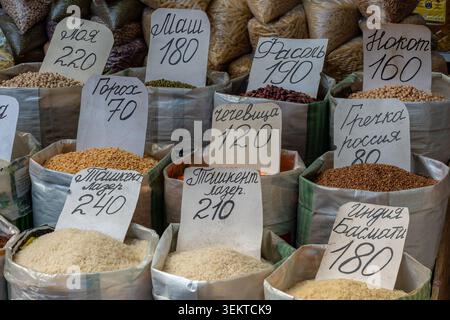 Große offene Säcke gefüllt mit verschiedenen Reissorten, Linsen und Bohnen mit handgeschriebenen Preisschildern in kyrillischer Sprache auf dem Bischkek Markt. Stockfoto