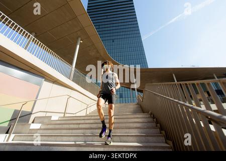 Der muskulöse Läufer steigt in einer belebten städtischen Umgebung unter hellem Sonnenlicht hinab. Sein Fokus und seine Geschwindigkeit sind offensichtlich. Stockfoto
