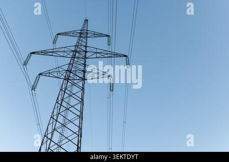 Stromleitungen erstrecken sich zwischen hohen Türmen unter blauem Himmel und zeigen einen Teil des heute genutzten Energieverteilungssystems. Stockfoto