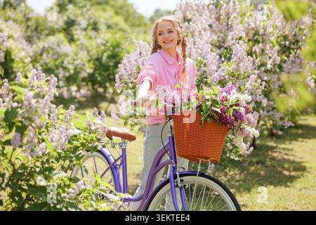 Eine fröhliche Frau fährt mit dem Fahrrad durch einen lebendigen Blumengarten, genießt die Schönheit der Natur und trägt einen Korb voller frischer Blüten Stockfoto