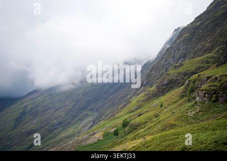 Dramatische Aussicht auf steile Berghänge, die teilweise von tief hängenden Wolken und dickem Nebel im Glencoe Valley, Schottland, verborgen sind Stockfoto