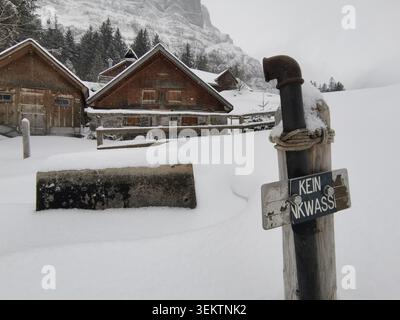 Schließen Sie einen Holzpfosten mit einem deutschsprachigem Schild mit der Aufschrift kein Trinkwasser neben einem tief verschneiten Holzchalet-Dorf im Winter Stockfoto