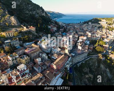 Blick aus der Vogelperspektive auf die historische Altstadt von Taormina mit ihren Terrakotta-Dächern auf einer Klippe mit Blick auf das blaue Mittelmeer Taormina, Stockfoto