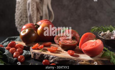 Eine stimmungsvolle, rustikale Lebensmittelfotografie mit einer Auswahl an lebendigen Erbstücken und Kirschtomaten, in Scheiben geschnitten und ganz, auf einem echten Holzschnitt Stockfoto