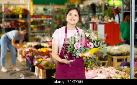 Asiatische Blumenläuferin, die im Blumengeschäft Blumenstrauß mit Rosen und Gerberas zubereitet Stockfoto