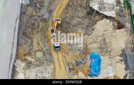 Aus der Vogelperspektive eines Baggers, der auf einer schlammigen Baustelle Boden in einen Müllwagen lädt, mit einem Arbeiter in der Nähe in Avcilar, Istanbul, Turkiye. Stockfoto