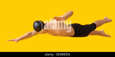 Männlicher Schwimmer in schwarzer Badekappe und Schutzbrille, die einen Freestyle-Schlag auf hellgelbem Hintergrund ausführen, sportlicher Mann in Badehose, der in A schwimmt Stockfoto