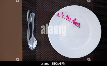 Flacher, sauberer, weißer Keramikteller von oben nach unten, geschmückt mit anmutigem rosafarbenen mexikanischen Kriechblüten (Chain of Love). Gepaart mit einem Silber für Stockfoto
