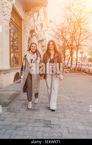 Frauenfreundschaft Herbst spazieren durch die Straßen der Stadt, während zwei fröhliche Begleiter in stilvollen, legeren Outfits goldene Sonnenuntergänge genießen Stockfoto