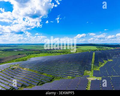 Ein Solarfeld erstreckt sich über eine grüne Landschaft. Die Tafeln sind in Reihen an einem Hang angeordnet. Der Himmel ist hell mit weißen Wolken. Die Szene Stockfoto