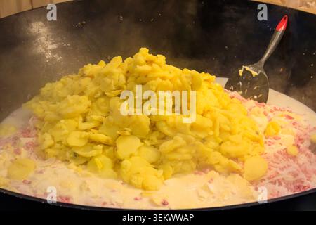 Zubereitung von Tartiflette, ein traditionelles französisches Gericht mit Jakobskartoffeln, Speck und Käse, in großem Kessel Stockfoto