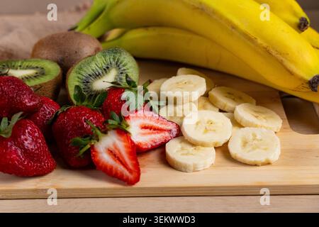 Nahaufnahme von frischen Erdbeeren, Bananen und Kiwi auf Holzschneidebrett angeordnet, symbolisiert gesunde Ernährung, Ernährung und buntes Obstsortiment Stockfoto