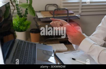 Frau, die Handgelenkschmerzen hat, weil sie im Heimbüro an einem Laptop arbeitet Stockfoto
