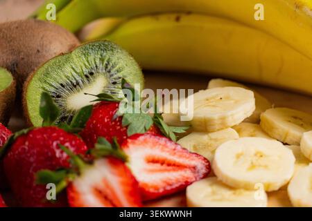 Nahaufnahme von frischen Erdbeeren, Bananen und Kiwi auf Holzschneidebrett angeordnet, symbolisiert gesunde Ernährung, Ernährung und buntes Obstsortiment Stockfoto