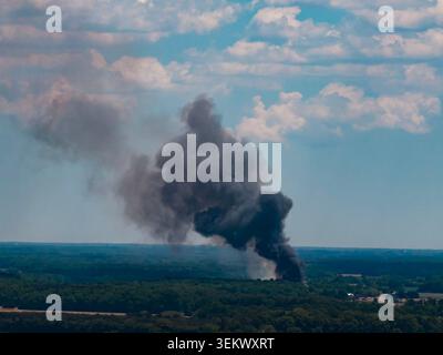 Wildfeuerrauch steigt über Wald auf. Wildfeuerfedern bedecken ländliche Bäume. Wildfeuer-Gefahr verdunkelt den Sommerhimmel. Wildfeuer-Dunst füllt den Horizont. Stockfoto