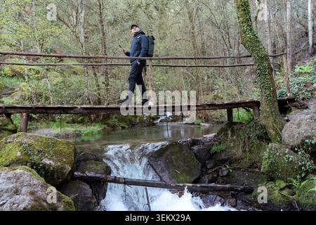 Mann, der über eine rustikale Holzbrücke läuft, während er einen üppig grünen Waldweg erkundet Stockfoto