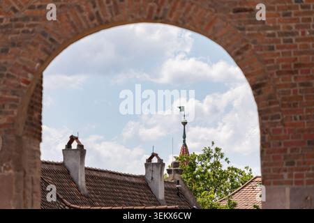 Mittelalterlicher Backsteinbogen, der historische Dächer umrahmt, und ein Turmturm unter Wolken in der Nürnberger Altstadt, Bayern, Deutschland. Stockfoto