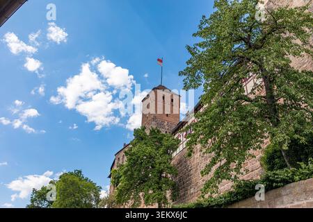 Mittelalterlicher Turm mit Fahne über Festungsmauern und grünen Bäumen auf Schloss Nürnberg in Bayern an einem sonnigen Tag heute. Stockfoto