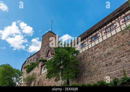 Mittelalterlicher Turm mit Fahne über Festungsmauern und grünen Bäumen auf Schloss Nürnberg in Bayern an einem sonnigen Tag heute. Stockfoto