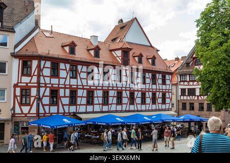 Historische Fachwerkhäuser säumen einen belebten Platz mit Besuchern in der Nürnberger Altstadt. Stockfoto