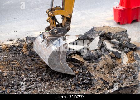 Nahaufnahme eines gelben Baggerlöffels, der an einer Straßenbaustelle bricht und alten Asphalt ausheben kann Stockfoto