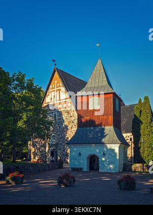 Espoo, Finnland - 26.07.2020: Historische Steinkirche mit rotem hölzernem Glockenturm und kunstvollem weißem Giebel unter hellem Sommersonnenlicht Stockfoto