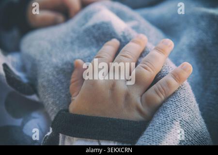 Ingå, Finnland - 19.06.2021: Zarte Makroaufnahme der Hand eines Babys, die sich an eine strukturierte graue Wolldecke bei weichem Tageslicht schmiegt Stockfoto