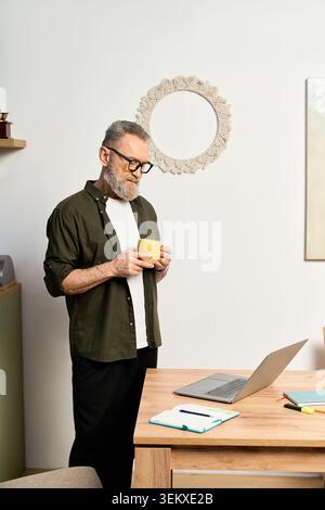 Ein älterer Mann mit Brille und Bart entspannt sich zu Hause, während er Tee in seiner stilvollen Wohnung schlürft. Stockfoto