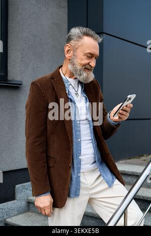 Ein hübscher älterer Mann überprüft sein Handy und nimmt die Energie einer modernen Stadt auf. Stockfoto